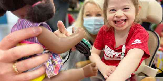 A little girl with blonde hair and a big smile on her face playing with an interactive doll using a button switch