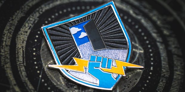 Everyone Can Play collectable pin is a shield with an open door to the sky in the background and a light blue fist holding a yellow lightning bolt in the foreground