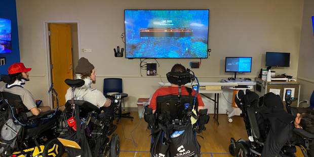 four young men playing a video game on a large screen mounted on the wall at the front of the room