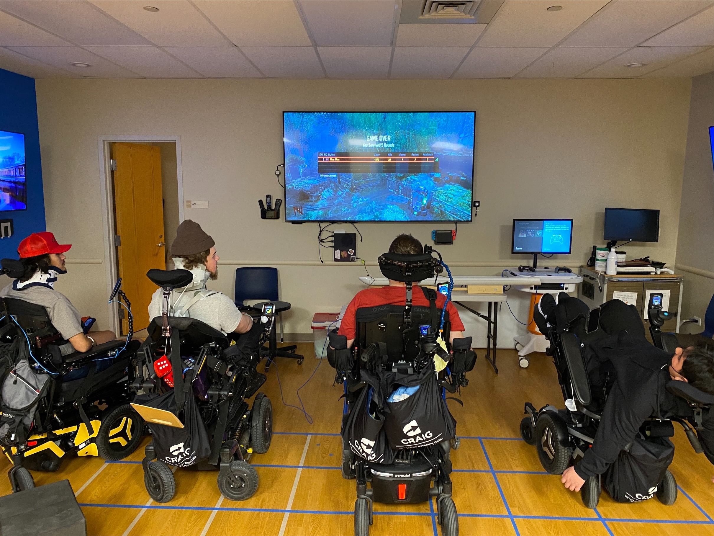 four young men playing a video game on a large screen mounted on the wall at the front of the room