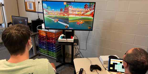 two people playing a video game on a large screen at the front of the room. Photo provided by Ability KC.