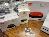 AbleGamers partnerships - Craig Hospital 3 boxes, 3 different switches green jelly bean switch, microLight and a Big Red sitting on a wooden table top with an ablegamers sticker in the center