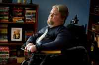 Steven Spohn, AbleGamers Chief Operating Officer sitting in front of a bookshelf full of books