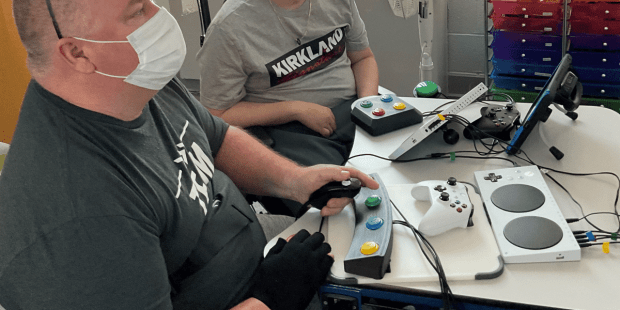 two individuals playing a video game, being social, and not isolated, using several different switches and adaptive controllers