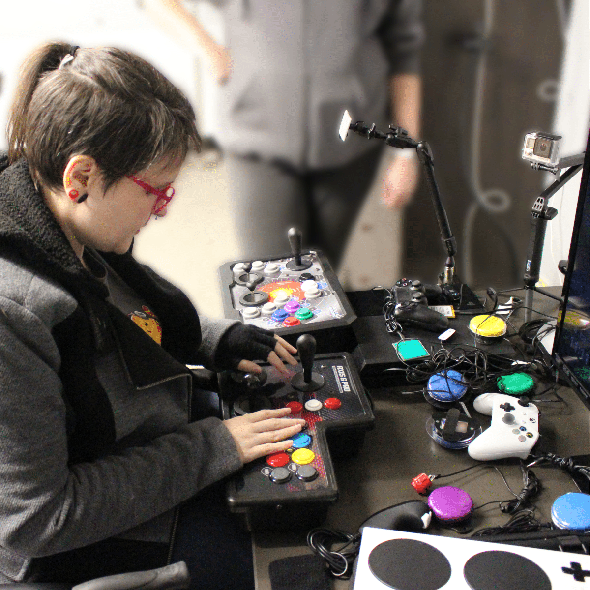 a young woman looking at several different adaptive controllers, switches and buttons. Support community and Inclusion, host a fundraiser