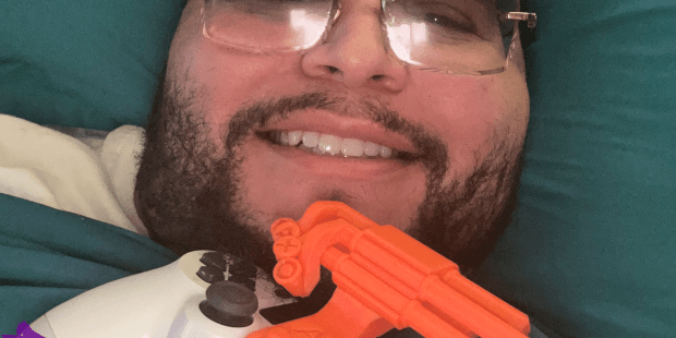 A photo of Elvin who has dark hair, a beard and is wearing glasses, and his Controller with a 3D-printed one-handed snap-on device