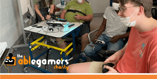Three individuals playing a video game together and another indivdual standing in the background at Powered by AbleGamers partner Ability KC- Global Accessibility Awareness Day May 16, 2024
