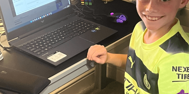 Husdon, a young man born with a limb difference looking at the camera with his new gaming laptop he just got.