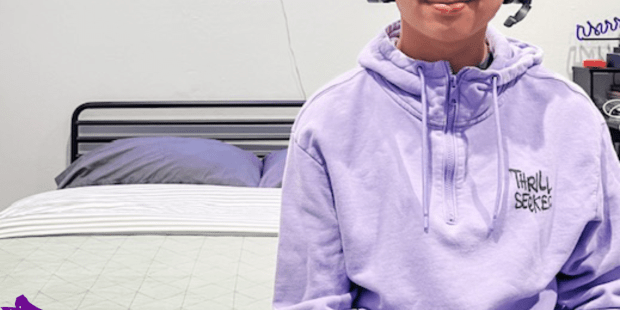 A photo of Isaiah he is wearing a purple hoodie and black headphones after working with AbleGamers to find the right adaptive gaming controller