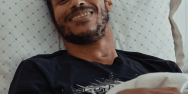 Jose, a young man with a light beard in bed smiling at the camera.
