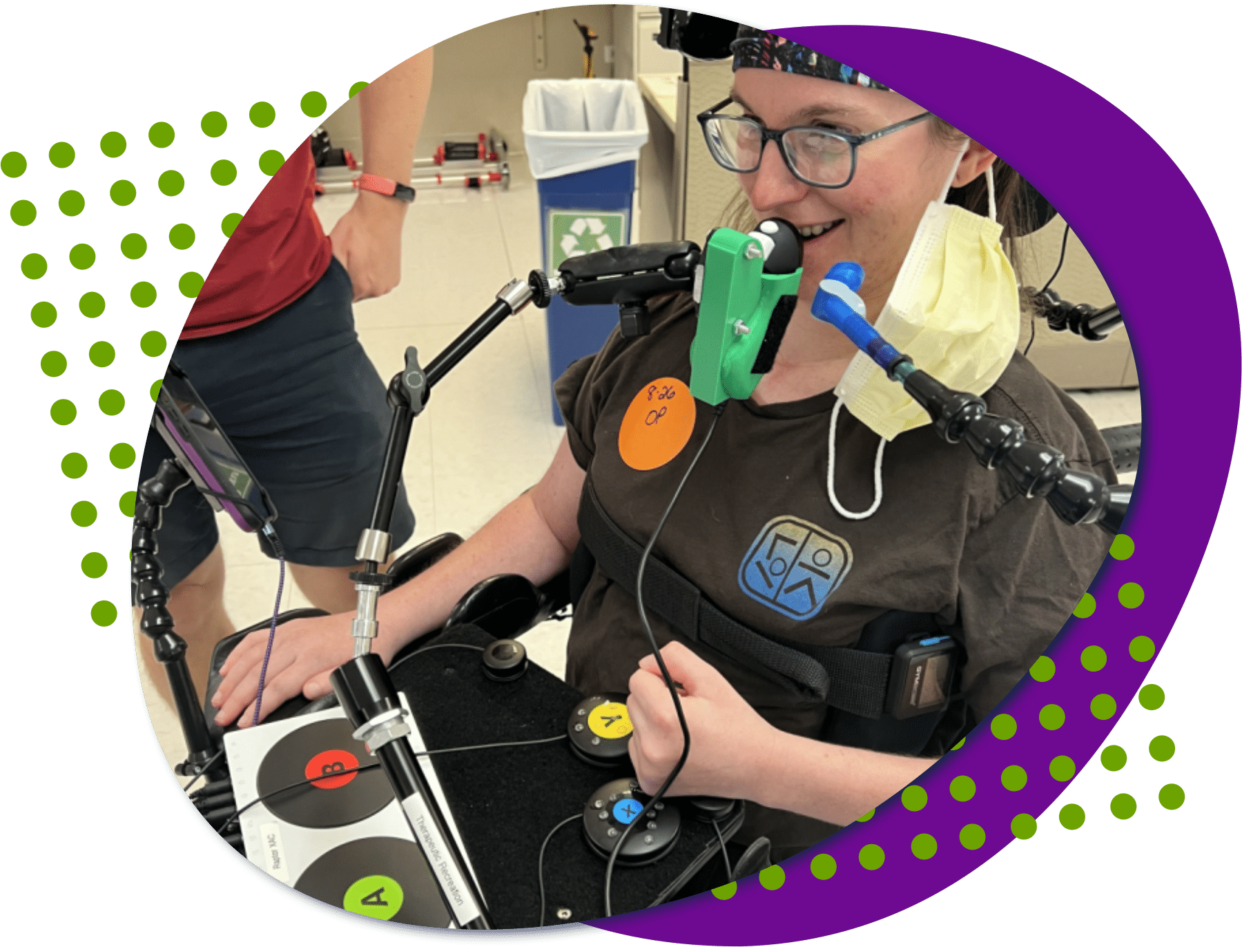 an image of a young woman, she is smiling and using several adaptive gaming devices to play a video game