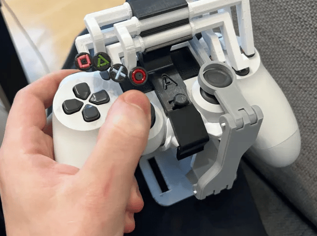 A white PlayStation 4 controller with hard plastic pieces attached. The X, O, Square, and Triangle icons are attached to the end of the plastic.