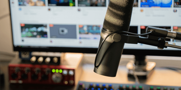 An image of a microphone, keyboard and computer screen on a table or desk. Possibly video Game Streaming.