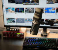 An image of a microphone, keyboard and computer screen on a table or desk. Possibly video Game Streaming.